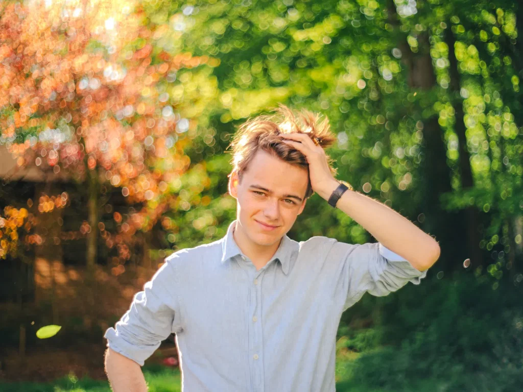 Jonge man met de hand in zijn haar, buiten in het groen in de herfstzon, gefotografeerd door Dies