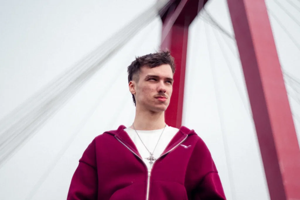 Jonge man in een rode hoodie voor de pilaren van een rode brug, gefotografeerd door Dies