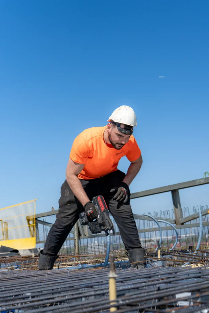 Vakman met oranje shirt en helm aan het werk op een bouwplaats, gefotografeerd door Dies